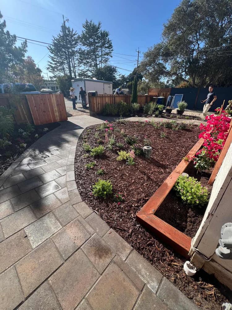 Curved paver path with a wood fence, gate, and raised planter bed