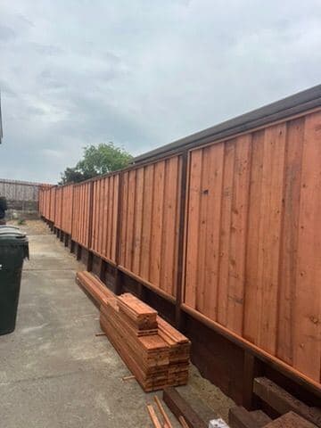Redwood privacy fence under construction with stacked boards nearby