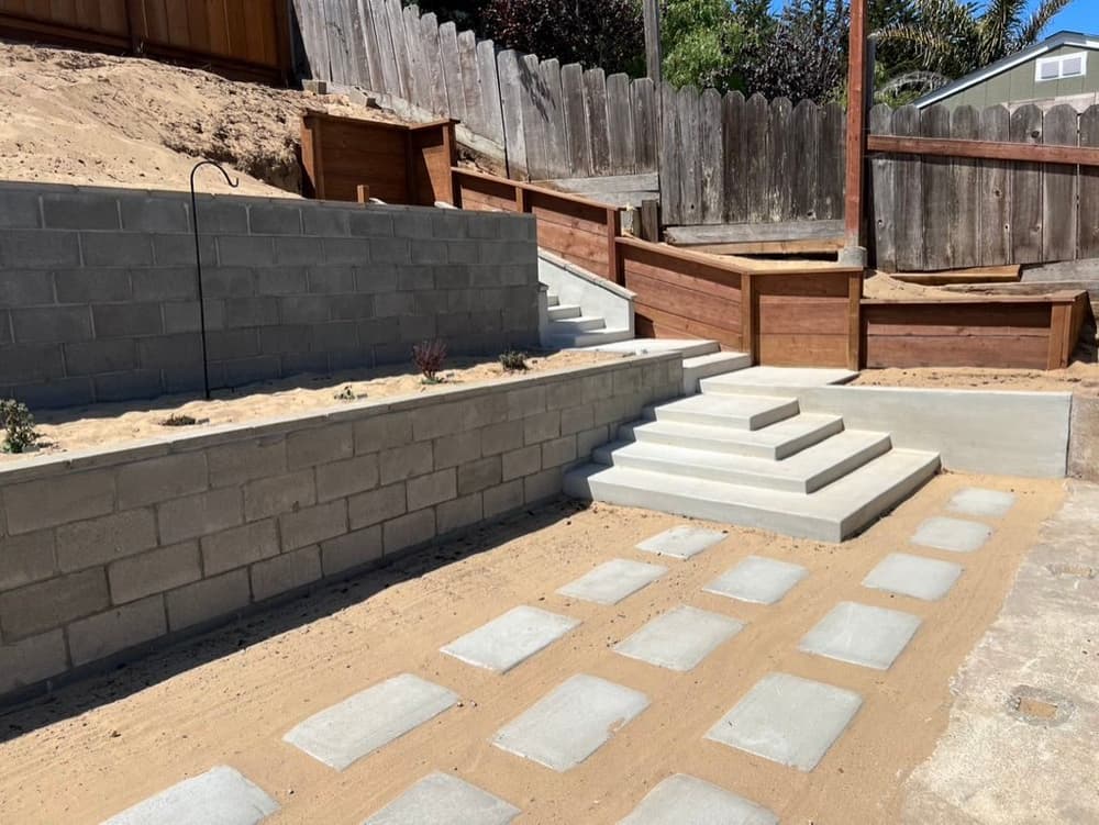 Block retaining wall with concrete steps and square stepping pads set in sand